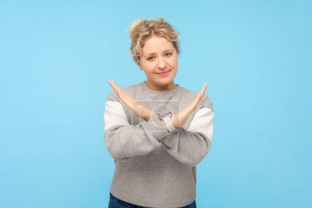 Photo for Portrait of blonde woman standing with crossed hands showing no way gesture asking to stop something, wearing gray sweatshirt. Indoor studio shot isolated on blue background. - Royalty Free Image