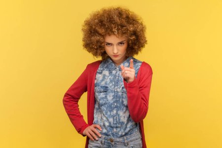 Photo for Portrait of serious strict woman with Afro hairstyle raising her finger up, warning you, scolding, has disapproval expression. Indoor studio shot isolated on yellow background. - Royalty Free Image