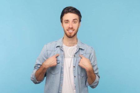 Photo for I can handle it. Assertive determined man points at himself, feels proud and brags about own achievements, proposes own help, wearing denim shirt. Indoor shot isolated on blue background. - Royalty Free Image