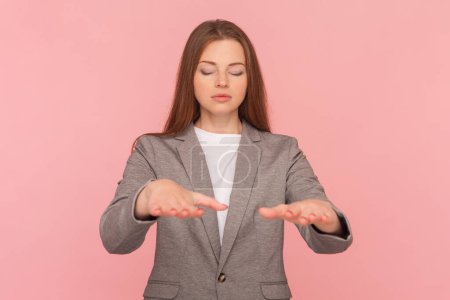 Photo for Portrait of blind unhealthy woman with brown hair standing with outstretched hand and closed eyes, trying to find way, wearing business suit. Indoor studio shot isolated on pink background. - Royalty Free Image