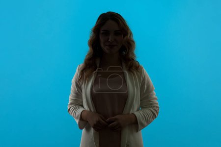 Photo for Anonymous person, no name. Silhouette portrait of woman with wavy hair hiding face in shadow, human identity, wearing white shirt. Indoor studio shot isolated on blue background. - Royalty Free Image