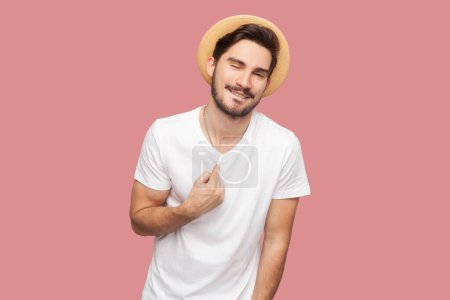 Photo for Portrait of delighted surprised bearded man in T-shirt and hat standing points at himself, achieves awesome opportunity, has glad facial expression. Indoor studio shot isolated on pink background. - Royalty Free Image