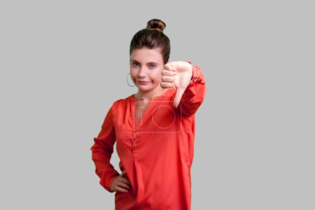 Photo for Portrait of displeased sad unhappy woman with bun hairstyle showing dislike gesture disapproval sign, negative feedback, wearing red blouse. Indoor studio shot isolated on gray background. - Royalty Free Image
