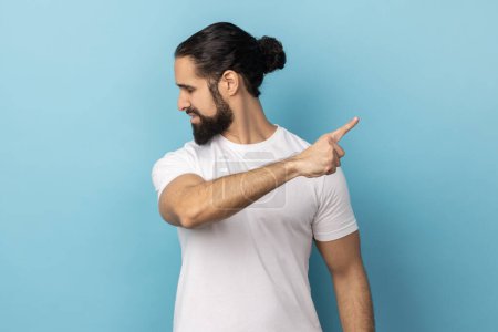 Photo for Get out. Portrait of man with beard wearing white T-shirt pointing away, scolding for bad result and showing exit, ordering to leave. Indoor studio shot isolated on blue background. - Royalty Free Image