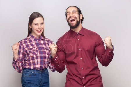 Photo for Portrait of joyful cheerful extremely happy young adult woman and man standing together clenching fists, celebrating victory, rejoicing. Indoor studio shot isolated on gray background. - Royalty Free Image