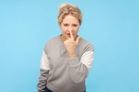 Photo for Portrait of dishonest blonde woman pointing at her nose, saying about fake situation, falsehood, wearing gray sweatshirt. Indoor studio shot isolated on blue background. - Royalty Free Image