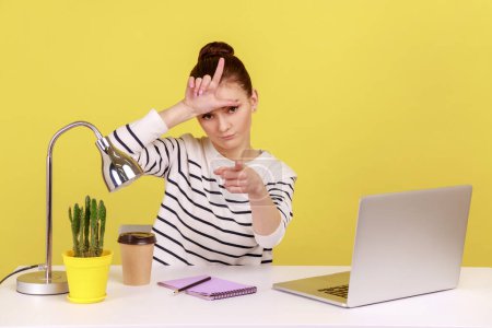 Photo for You are fired. Angry woman sitting at workplace, showing loser gesture, pointing to camera, blaming for unsuccess, failed project and lost job. Indoor studio studio shot isolated on yellow background. - Royalty Free Image