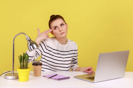 Photo for Depressed overworked woman office worker holding fingers near temple imitating gun shot, feeling stress and pressure because of work problems. Indoor studio studio shot isolated on yellow background. - Royalty Free Image