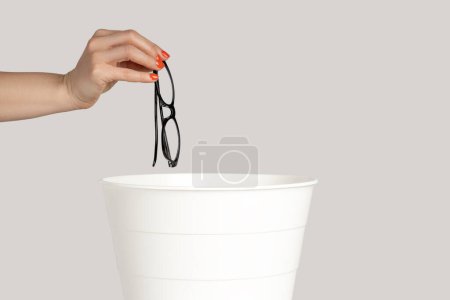 Closeup of woman hand trowing away glasses after eyesight treatment. Indoor studio shot isolated on gray background.