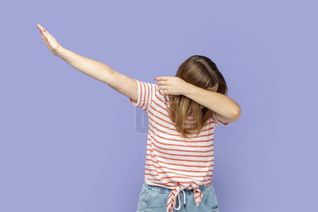Retrato de una rubia anónima de cabello oscuro con una camiseta a rayas de pie en pose de baile, meme de internet, celebrando el éxito. Estudio interior plano aislado sobre fondo púrpura.