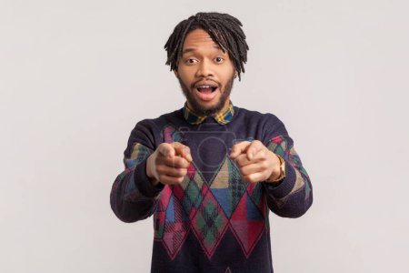 Portrait of surprised astonished african-american man with dreadlocks and beard pointing at camera with both index fingers, looking at camera. Indoor studio shot isolated on gray background.