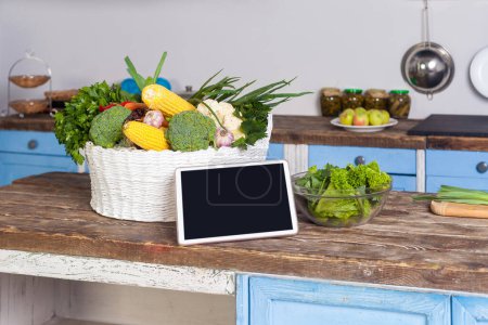 Photo for Tablet with blank screen copy space for advertisement of healthy vegetarian low-calorie diet, food recipes, menu and blog, fresh vegetables on wooden table in modern kitchen. - Royalty Free Image