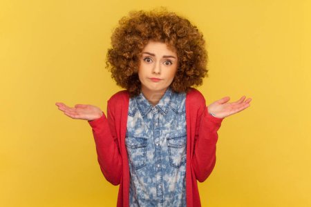 Photo for Portrait of puzzled clueless woman with Afro hairstyle receives strange offer, shrugging shoulders with hesitation, feels doubt. Indoor studio shot isolated on yellow background. - Royalty Free Image