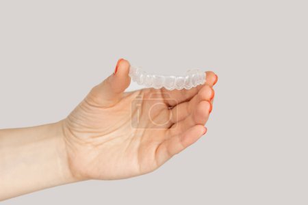 Closeup of woman hand showing invisible orthodontics cosmetic aligners. Indoor studio shot isolated on gray background.