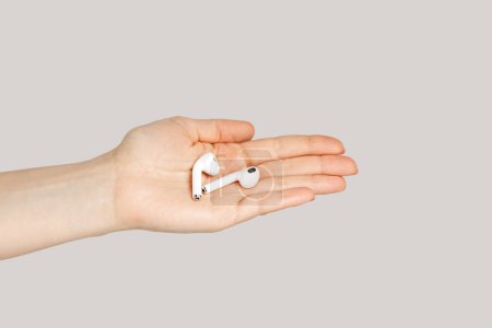 Foto de Primer plano de la mano de la mujer que muestra auriculares blancos para escuchar música, dispositivo digital. Estudio interior plano aislado sobre fondo gris. - Imagen libre de derechos