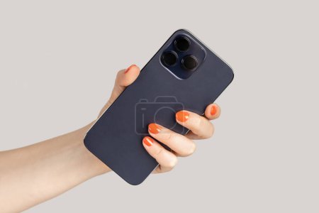 Photo for Closeup of woman hand holding smartphone, showing back of mobile phone. Indoor studio shot isolated on gray background. - Royalty Free Image