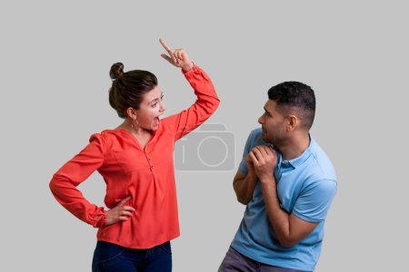 Portrait of couple standing together woman arguing her husband raised finger screaming to scared man family problems. Indoor studio shot isolated on gray background.