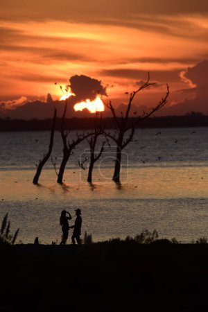 Foto de Recién casados en una boda romántica, de vacaciones, en su luna de miel, en un paisaje de una puesta de sol naranja. - Imagen libre de derechos