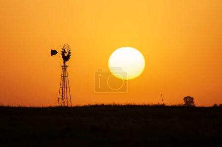 Foto de Molino de viento en el campo al atardecer naranja, Pampa, Patagonia, Argentina. - Imagen libre de derechos