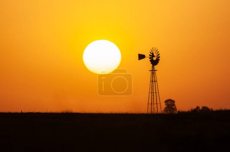 Windmill in countryside at orange sunset, Pampas, Patagonia, Argentina.