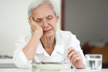 Foto de Disappointed old elderly people eating overnight food,she's sick of food,tired of eating same food,lacking flavor,Asian senior woman suffering from anorexia,loss of appetite,diet and nutrition concept - Imagen libre de derechos