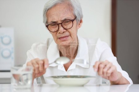 Foto de Disappointed old people looking at food on dish,eating leftovers,monotonous overnight food,tired expression feel bad,disgusted,Asian senior woman having lack of appetite,diet,  nutrition of elderly - Imagen libre de derechos