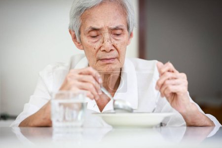 Kranke asiatische Seniorin, die an Magersucht leidet, sich beim Essen langweilt, weniger isst oder Schluckbeschwerden hat, an Dysphagie leidet, alte ältere Patientin mit Appetitlosigkeit, Ernährung und Gesundheitsfürsorge