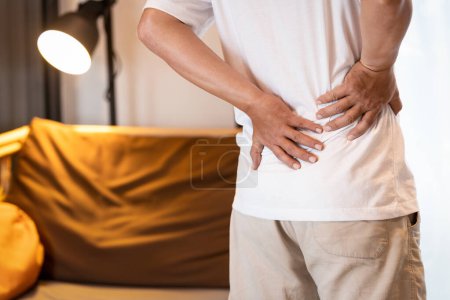 Hombre asiático triste con dolor de espalda después del sueño, personas estresadas que sufren de dolor de espalda baja, hernia discal lumbar, tensión musculotendinosa, tocándose la espalda con las manos, cuidado de la salud, concepto médico