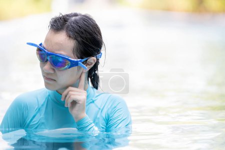 Foto de Chica asiática estresada tenía acúfenos, problema con el agua entrando en el canal auditivo mientras nadaba, personas hembras limpiando oídos después de bucear en la piscina, otitis externa, oído de nadador, concepto de cuidado de la salud - Imagen libre de derechos