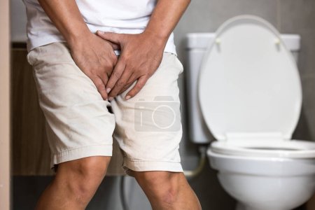 Asiatischer Mann mittleren Alters leidet an Dysurie, akuter Blasenentzündung, Harnwegsinfektion, Menschen, die im Schritt auf der Toilette stehen, Prostata-Problemen, Harnröhrenentzündung, schmerzhaftem oder erschwertem Wasserlassen