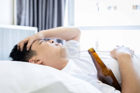 Photo for Hungover male suffer from severe headache in the morning after night out drinking,Drunk middle aged man hugging bottle of beer,lying on bed,having a hangover,pain in head,drinking an excess of alcohol - Royalty Free Image