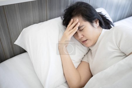 Kranke Frau mittleren Alters mit starken Migräne-Kopfschmerzen bleiben im Bett, Migräneattacke am Morgen, Probleme mit chronischer Schlaflosigkeit, Aufwachen mit Kopfschmerzen aus unzureichendem Schlaf oder schlaflose Nacht