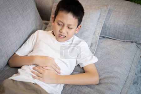 Niño asiático enfermo que sufre de gastritis, úlcera gástrica, dolor de estómago, inflamación del estómago y los intestinos, síntomas de gastroenteritis, infección de bacterias o virus, dolor, dolor en el abdomen