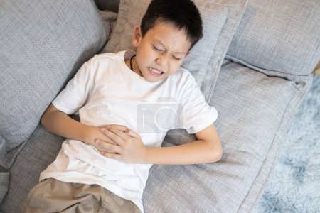 Malade enfant asiatique garçon souffrant de maux d'estomac, tenant son ventre, douleur abdominale sévère, l'appendice devient enflammé et douloureux, maladie abdominale, appendicite aiguë, urgence médicale, concept de soins de santé