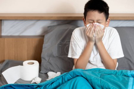 Kranker Junge, der an Grippe, Influenza-Virus, verstopfter Nase, laufender Nase, Blasen oder Wischen mit Seidenpapier, Atemwegserkrankungen, akuter Rhinopharyngitis, Fieber und Erkältung, Infektion, Krankheit leidet