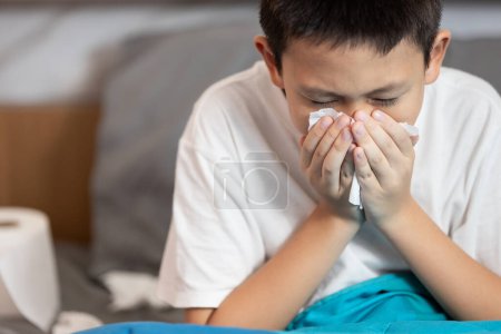 Sick child boy having allergies,hay fever,runny nose,sneezing,nasal congestion,blow the nose with tissue paper,inflammation of a nasal sinus,allergic rhinitis,seasonal allergy or dust,air pollution
