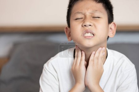 Niño asiático tocándose el cuello, pérdida de la voz, ronquera, voz ronca de laringitis o dolor de garganta, dificultad para tragar, irritación dentro de la garganta o enfermedad de amigdalitis, faringitis aguda