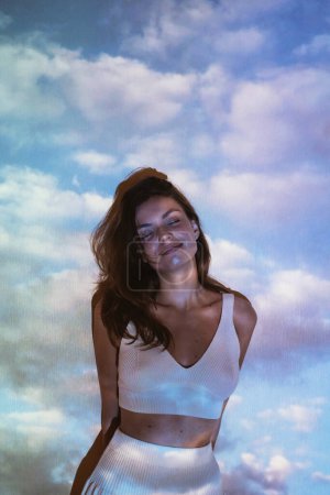 Téléchargez les photos : Jeune adulte belle femme z-gen avec des nuages image projetée sur elle avec projecteur. Photo de haute qualité - en image libre de droit