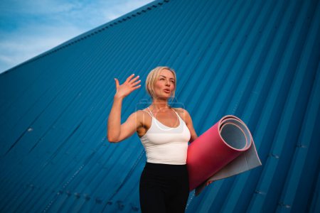 Photo for Middle age beautiful woman with sport mat outdoors on blue wall background. Hot weather. High quality photo - Royalty Free Image