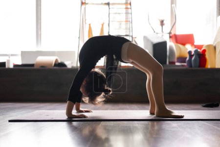 Small girl doing bridge stand exercise in the training studio. Yoga for kids, gymnastics class. Healthy physical development of a child. High quality photo