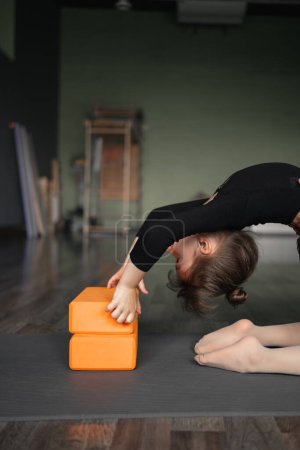 Preschool age child girl doing stretching exercises in dancing or yoga studio. Yoga blocks and sport mat. Back stretching flexibility. High quality photo