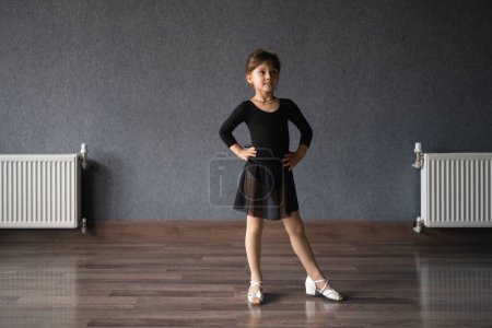 Téléchargez les photos : Enfant fille debout en costume de sport noir en studio de danse pendant la posture d'entraînement. 4 5 ans d'âge préscolaire. Développement physique sain. Photo de haute qualité - en image libre de droit