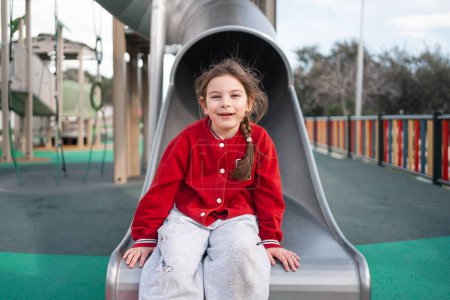 Ein glückliches Kind sitzt oben auf einer Rutsche auf einem Spielplatz, bereit für Spaß und Abenteuer. Hochwertiges Foto