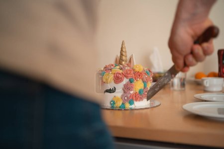 The magical moment of cutting into a colorful unicorn-themed cake, with swirls of pastel icing, during a family celebration. High quality photo