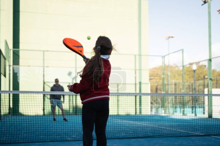 A focused young girl practices her paddle tennis skills on a vibrant blue court on a clear day. High quality photo
