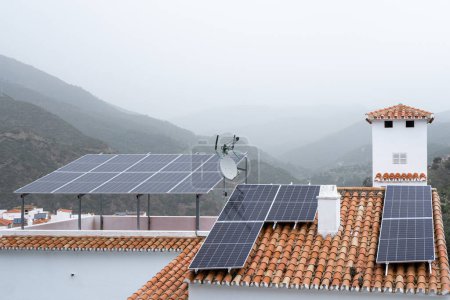 Vivir sostenible en un pueblo de montaña cubierto de niebla, con paneles solares en tejados de terracota aprovechando la energía renovable. Foto de alta calidad