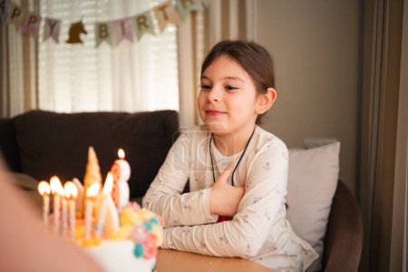 Ein Kind schließt die Augen, um einen Geburtstagswunsch zu formulieren, bläst Kerzen auf eine Einhorntorte, umgeben von fröhlicher Feierstimmung zu Hause. Hochwertiges Foto