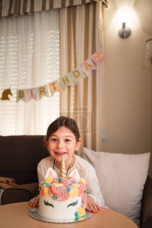 A young girl poses with a gleeful smile beside her magical unicorn birthday cake, ready to celebrate her special day with sweetness and joy. High quality photo