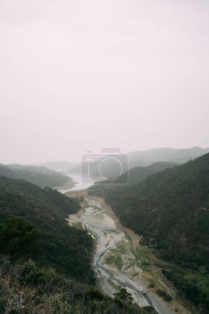 Une scène tranquille d'une rivière sinueuse traversant une vallée luxuriante, avec du brouillard recouvrant les collines lointaines et une maison solitaire visible. Photo de haute qualité