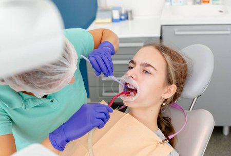 Concept of dental care. The process of installing orthodontic ceramic brackets. Close-up view of dentist's hands applying blue glue to patient's clean bottom teeth before attaching braces
